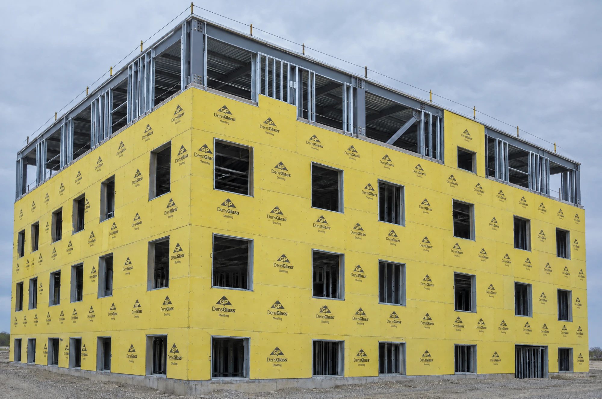 A four-storey steel-framed building wrapped in yellow DensGlass sheathing, with the top floor's steel studs still open