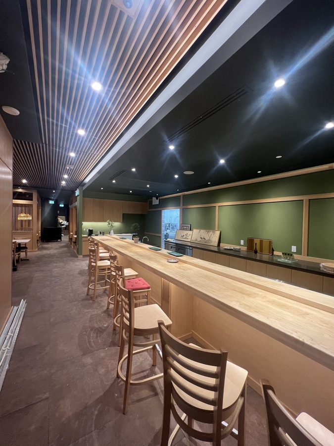 Bar seating along a wood counter under a slat ceiling and black bulkhead