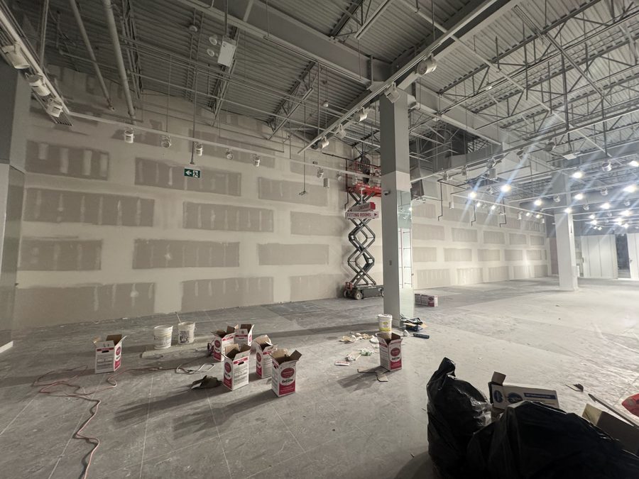 A long drywall wall with taped joints in a large open space, a scissor lift beside it