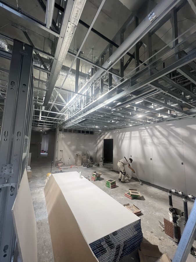 A stack of drywall board on the floor under completed steel ceiling framing