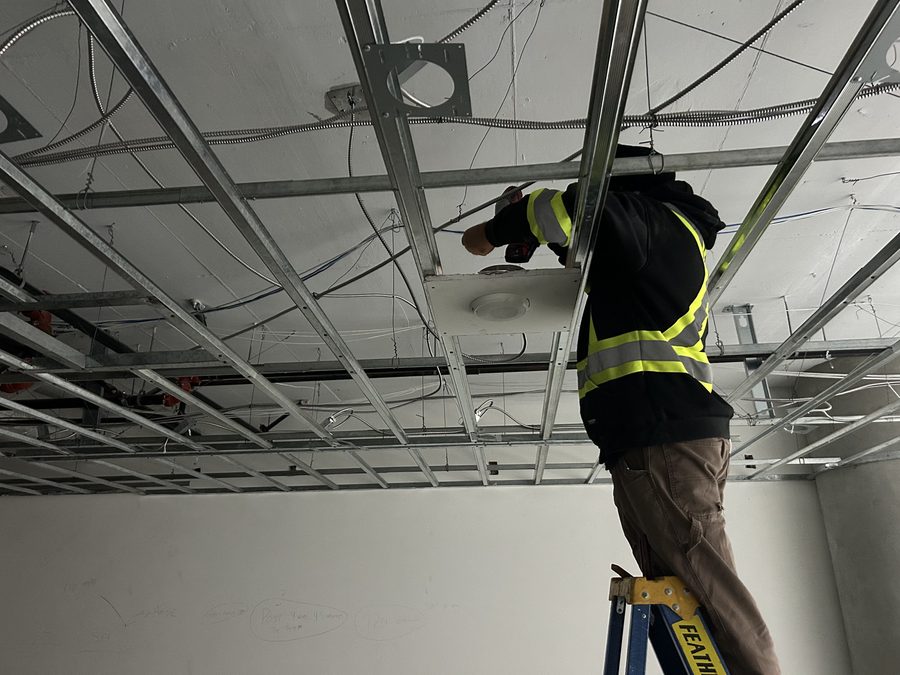 A worker in a hi-vis vest on a ladder installing a suspended ceiling grid