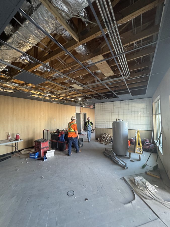 A suspended ceiling grid under an open wood roof structure with ductwork, crew working below