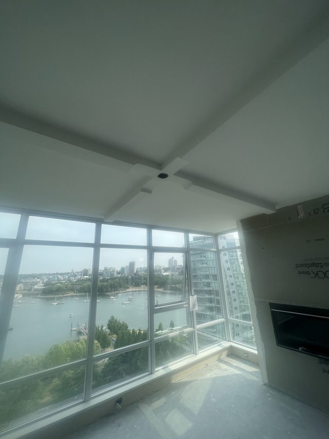 Two drywall soffits meeting at a corner above floor-to-ceiling windows with a water view
