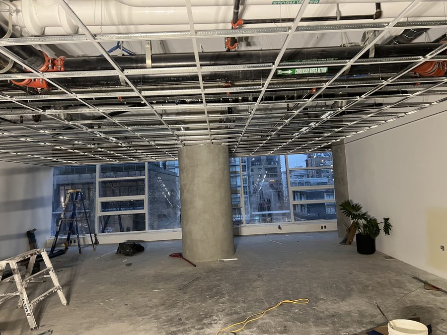 A suspended T-bar ceiling grid over an open office floor with a round column and windows