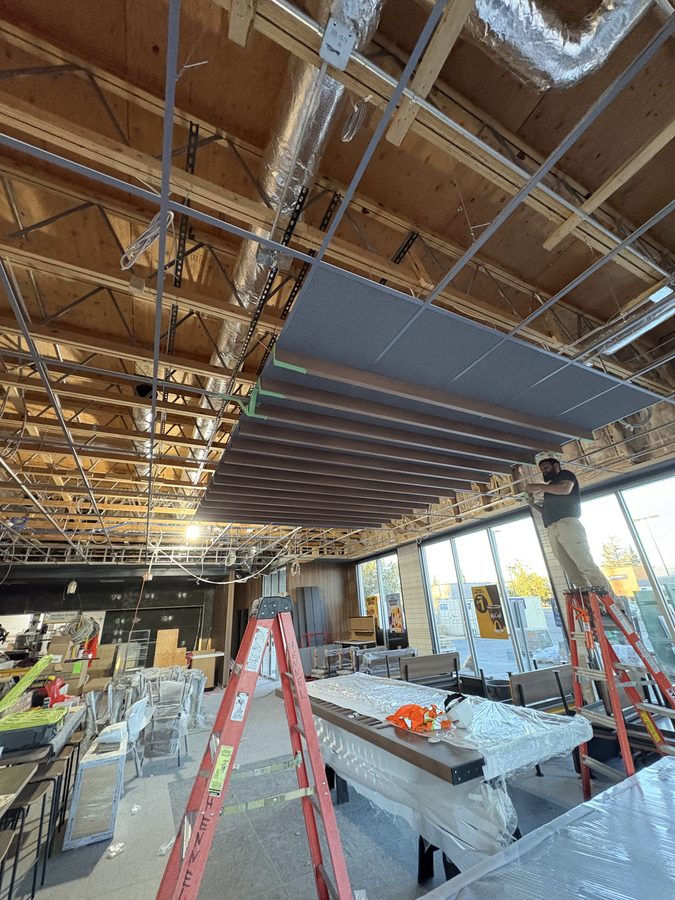 Ceiling panels being installed over a restaurant dining room, ladders and covered furniture below
