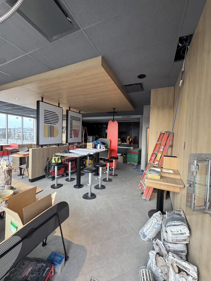 A restaurant dining room with a wood-wrapped bulkhead and T-bar ceiling during final fit-out
