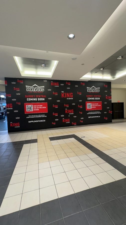 A drywall bulkhead ceiling with cove lighting over a retail entry with a branded hoarding wall