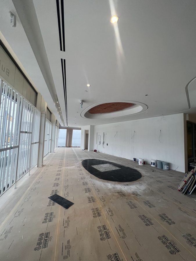 A long open room with a flush white ceiling, linear diffusers and a round recessed ceiling feature