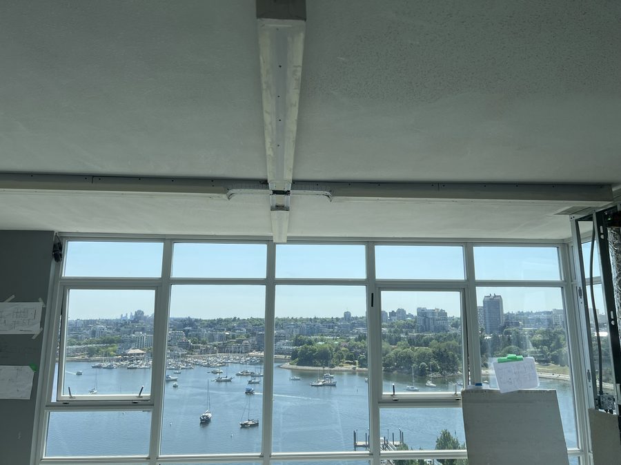 A drywall soffit running across the ceiling of a high-rise suite above floor-to-ceiling windows overlooking a marina