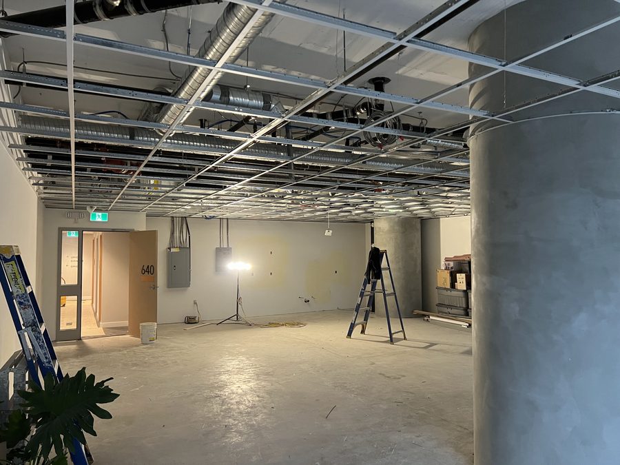 A T-bar ceiling grid being installed over an office floor around a round concrete column
